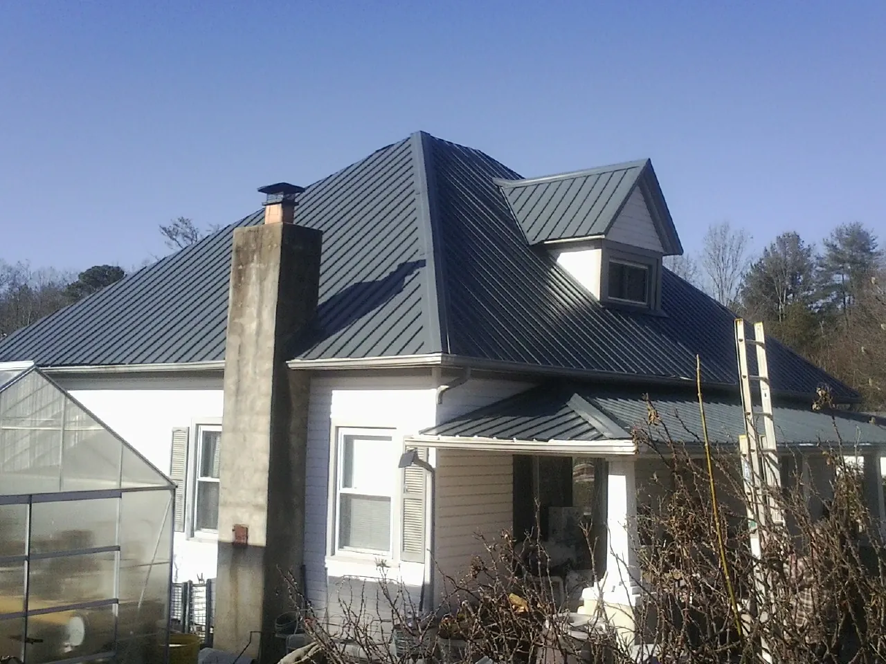 Dark blue standing seam metal roof on a white farmhouse with dormer — Slate & Tile Roof Repair by Roofing Brothers in Reston