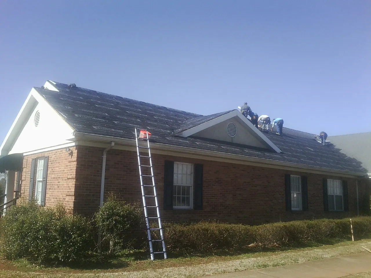 Crew tearing shingles off a brick ranch roof with a ladder set — Emergency Roof Repair work by our crew in Reston