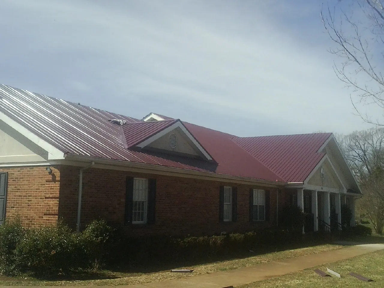Red metal roof with gabled entries on a long brick building, from a Hail Damage Roof Repair job in Reston